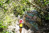 Bonita_Falls_064_06122020 - Julie and Tahia walking by a heavily-spray-painted rock on the final stretch up to Bonita Falls