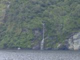 Doubtful_Sound_116_11252004 - A boat dwarfed by an ephemeral waterfall