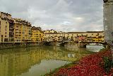 Florence_314_11212023 - More contextual look at the Ponte Vecchio reflected in the Arno River with some red flowers along one bank of the river and some incoming clouds threatening bad weather