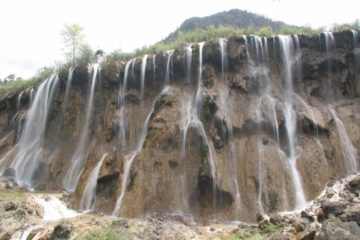 The Nuorilang Waterfall (诺日朗瀑布 [Nuòrìlǎng Pùbù]; Promising Bright Bay Waterfall) was nearby the road so Julie and I noticed that it tended to grab the attention of bus riders thereby earning it the...