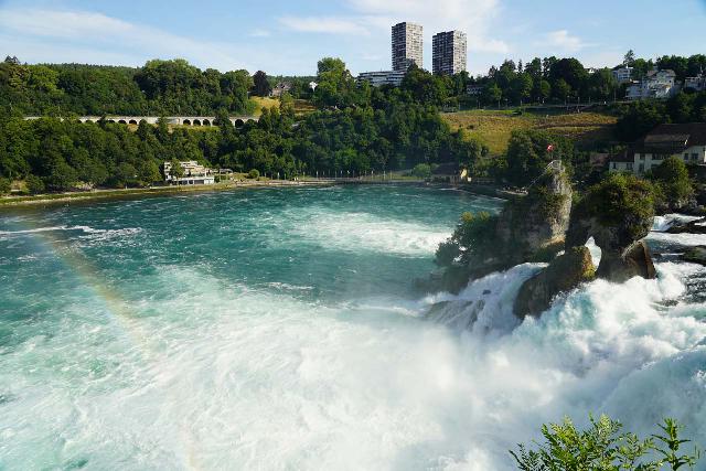 Rhine_Falls_060_06262025 - Looking across the Rhine Falls towards the middle island fronted by a smaller island with a natural arch in it along with a morning rainbow further downstream
