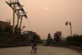 Spokane_Falls_005_08042017 - Julie and Tahia walking beneath the red globe sun against the thick smoke and the cable car infrastructure somewhere near Spokane Falls